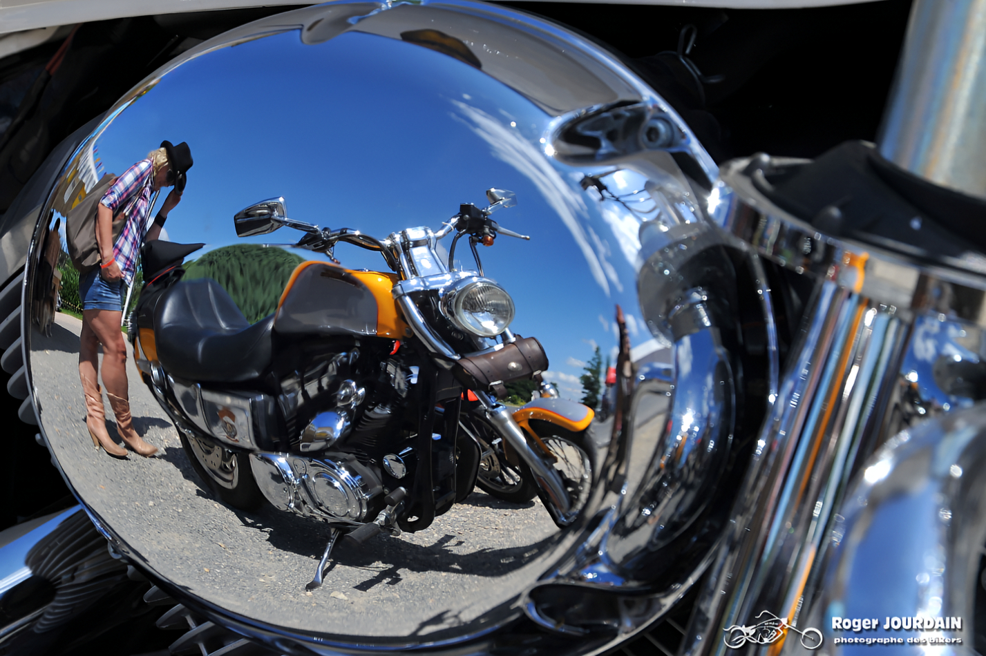 Reflet déformé d'une motarde en short et d'une moto dans le chrome d'un phare ou d'un carter d'une autre machine lors du Free Wheels.