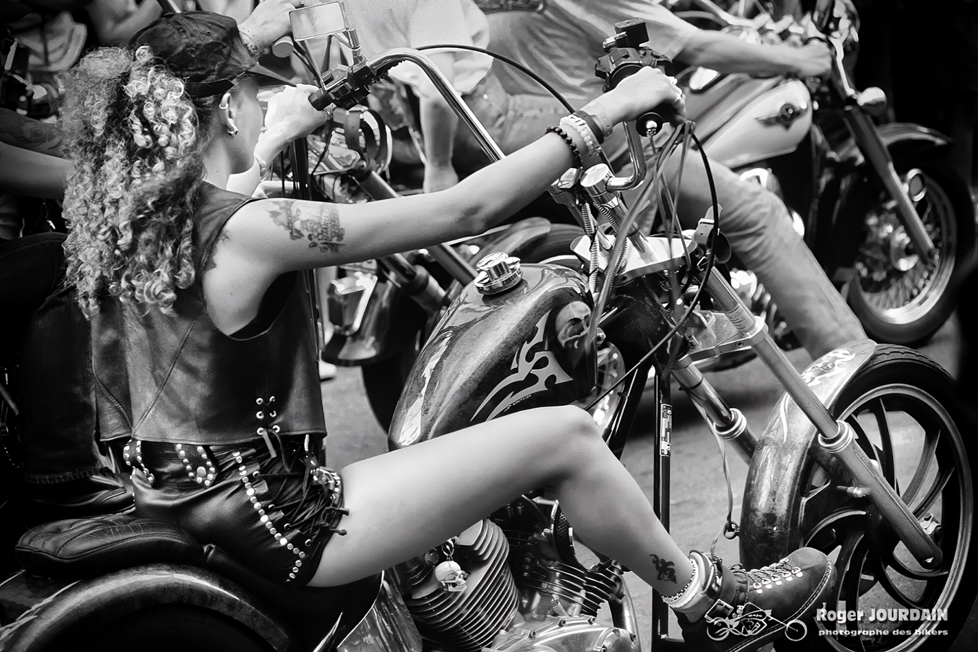 Jeune femme motarde avec tatouages et cheveux bouclés, assise sur une moto custom (chopper) lors du Free Wheels.