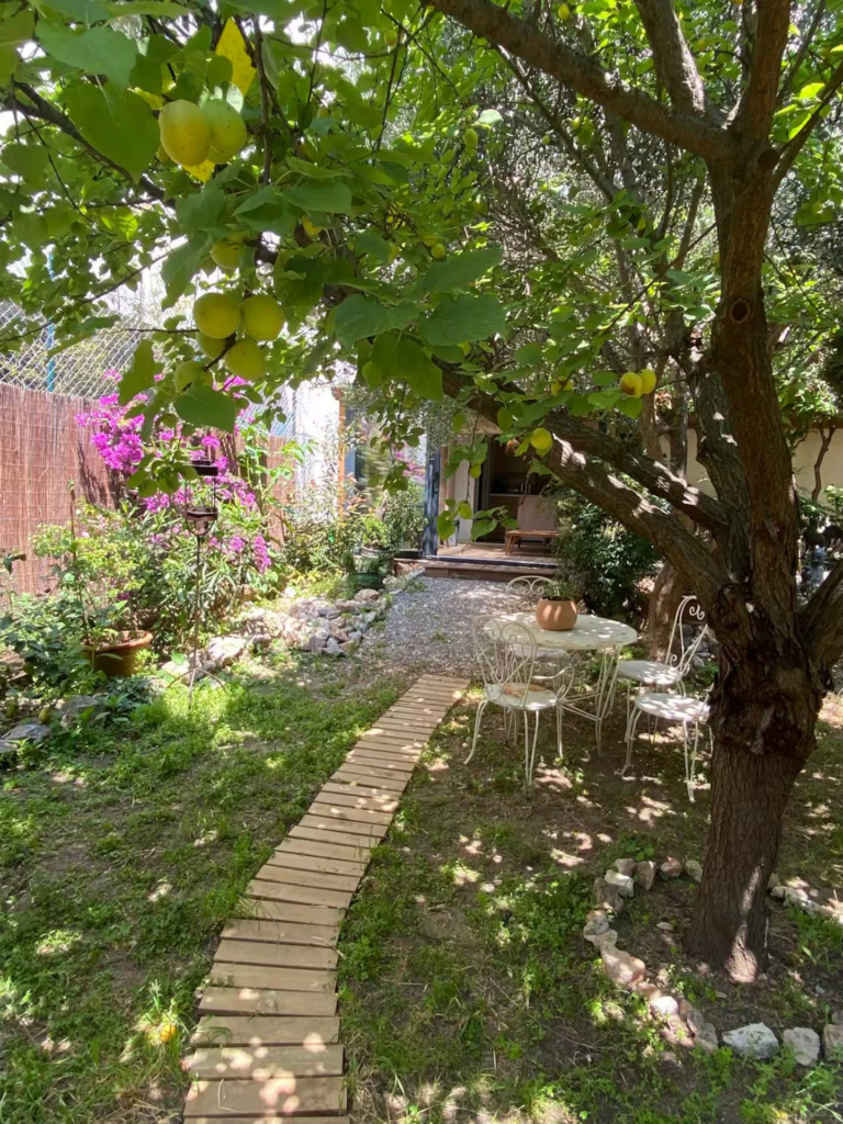 Jardin méditerranéen arboré avec allée en bois, table extérieure et arbres fruitiers dans un cadre paisible