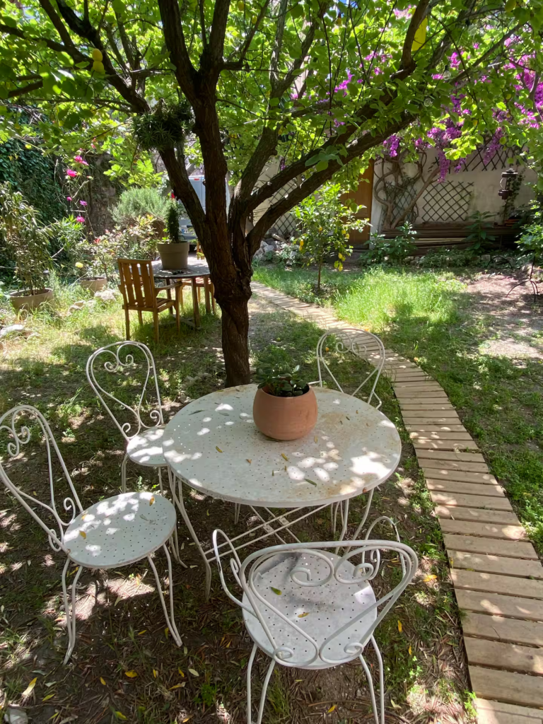 Salon de jardin sous un arbre dans un jardin méditerranéen ombragé avec allée en bois et espace détente