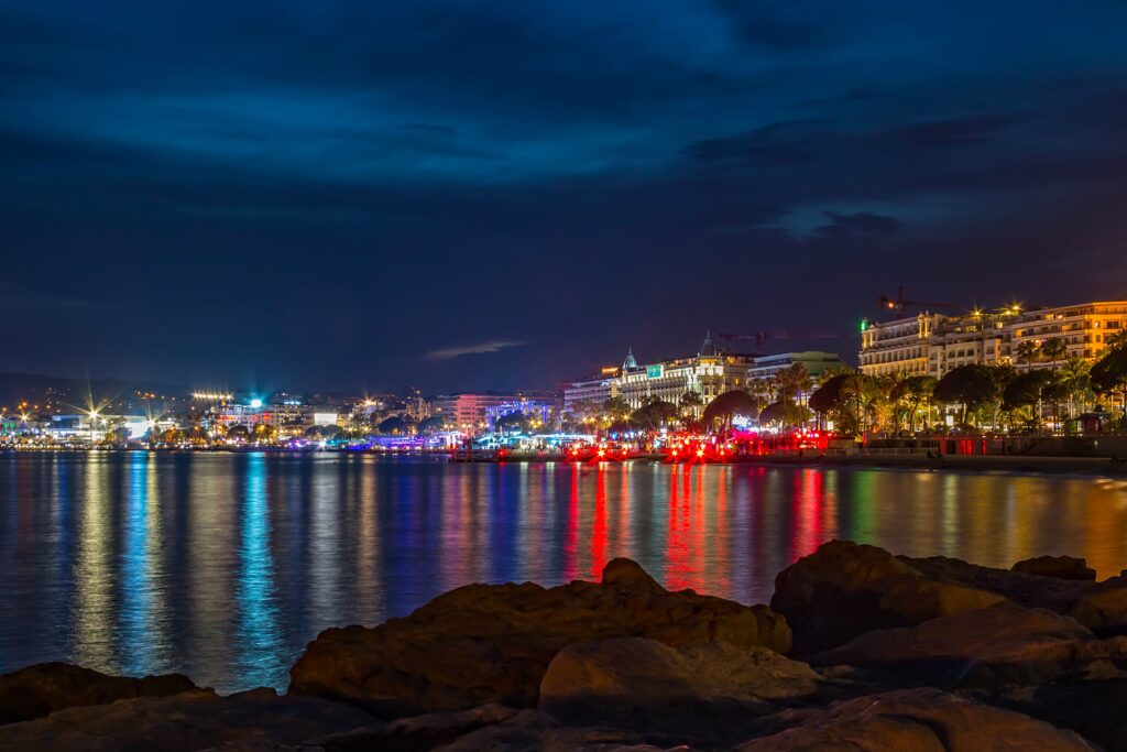 Cannes Croisette at night with luxury hotels, illuminated waterfront and reflections on the Mediterranean Sea.